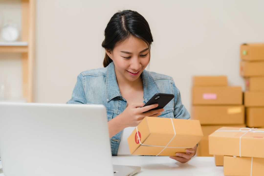 Eine junge Frau scannt ein Versandpaket mit ihrem Smartphone im Homeoffice.